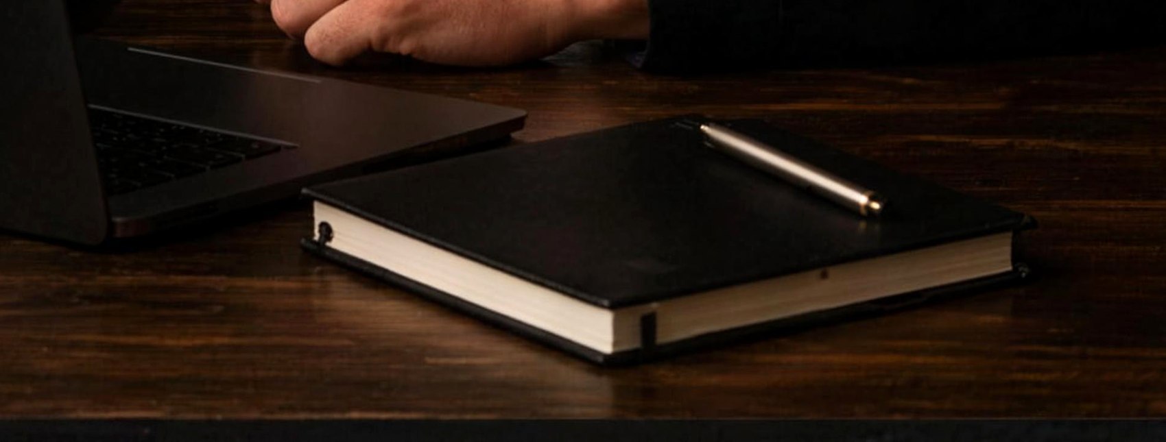 Workbench: laptop, notebook and pen on dark wood